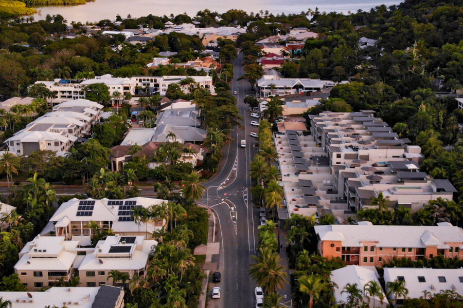 Aerial view of Macrossan Street with modern homes and palm-lined roads, surrounded by lush greenery in a serene tropical setting.