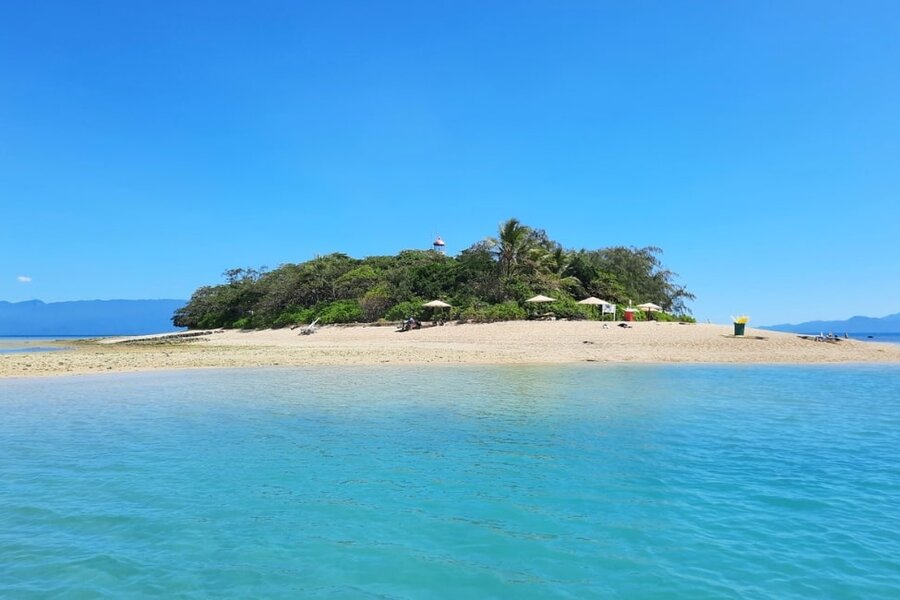 Low Isles with a sandy beach, lush greenery, and a distant lighthouse, surrounded by calm turquoise waters under a clear blue sky.